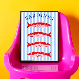 Puede incluir: Un cuadro enmarcado con la palabra "SARDINES" en la parte superior y cuatro ilustraciones de peces rojos sobre un fondo de rayas azules y blancas. El cuadro se muestra en una silla rosa sobre un fondo amarillo.