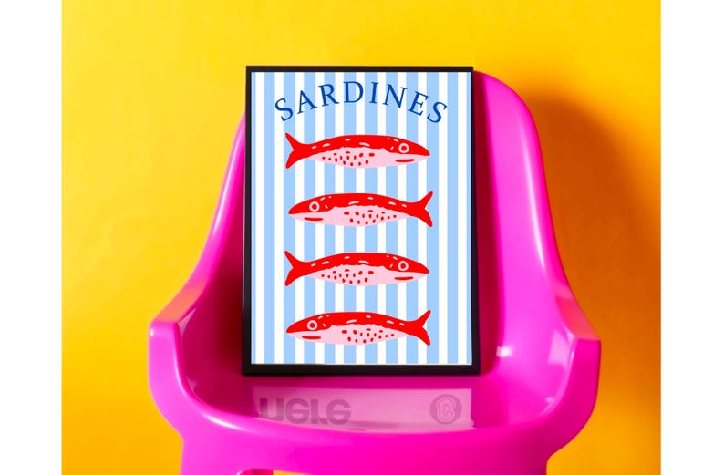Puede incluir: Un cuadro enmarcado con la palabra "SARDINES" en la parte superior y cuatro ilustraciones de peces rojos sobre un fondo de rayas azules y blancas. El cuadro se muestra en una silla rosa sobre un fondo amarillo.