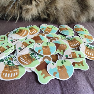 Pode incluir: Uma cole&ccedil;&atilde;o de adesivos coloridos com gatos de desenho animado com rostos sorridentes. Os gatos s&atilde;o retratados em v&aacute;rias poses, incluindo sentados em vasos de plantas, relaxando em prateleiras e relaxando em um fundo azul e verde. Os adesivos s&atilde;o perfeitos para adicionar um toque de fantasia a laptops, garrafas de &aacute;gua ou di&aacute;rios.