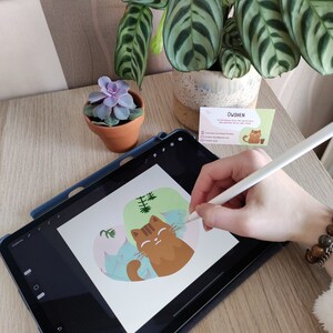 Pode incluir: Uma ilustra&ccedil;&atilde;o digital de um gato marrom com uma planta verde no fundo. O gato est&aacute; sendo desenhado em um tablet usando uma caneta.