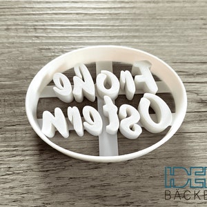 May include: White plastic cookie cutter with the words "Frohe Ostern" in a cursive font.