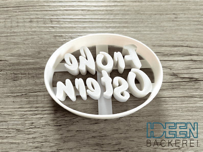 May include: White plastic cookie cutter with the words "Frohe Ostern" in a cursive font.