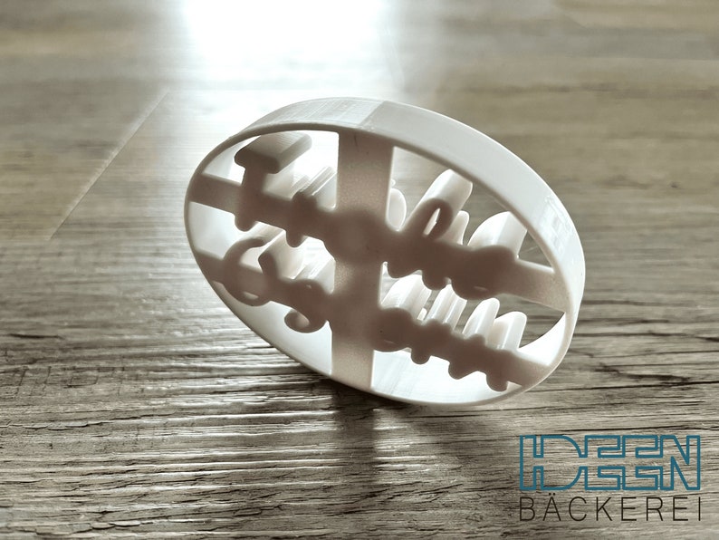 May include: White plastic cookie cutter shaped like an oval with the words "Hallo" and "Guten Appetit" cut out.