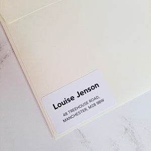 Könnte beinhalten: Weißer Umschlag mit einem weißen Etikett mit der Aufschrift "Louise Jenson, 48 Treehouse Road, Manchester, M28 9BW"