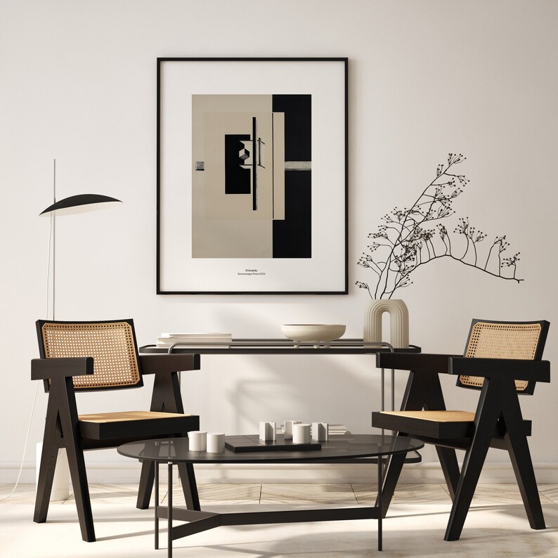 May include: A black and white abstract art print in a black frame hangs on a white wall above a black wooden table with two black chairs. A small white vase with a dried plant sits on the table.