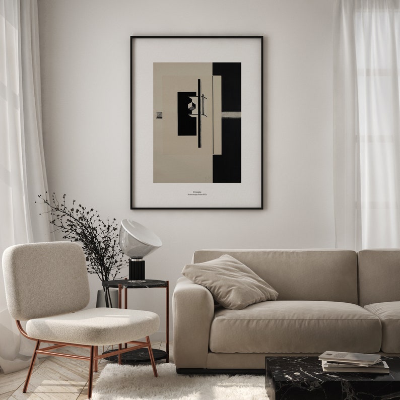 May include: A black and white abstract art print in a black frame hanging on a white wall above a beige sofa and a beige chair. The print features geometric shapes and lines.