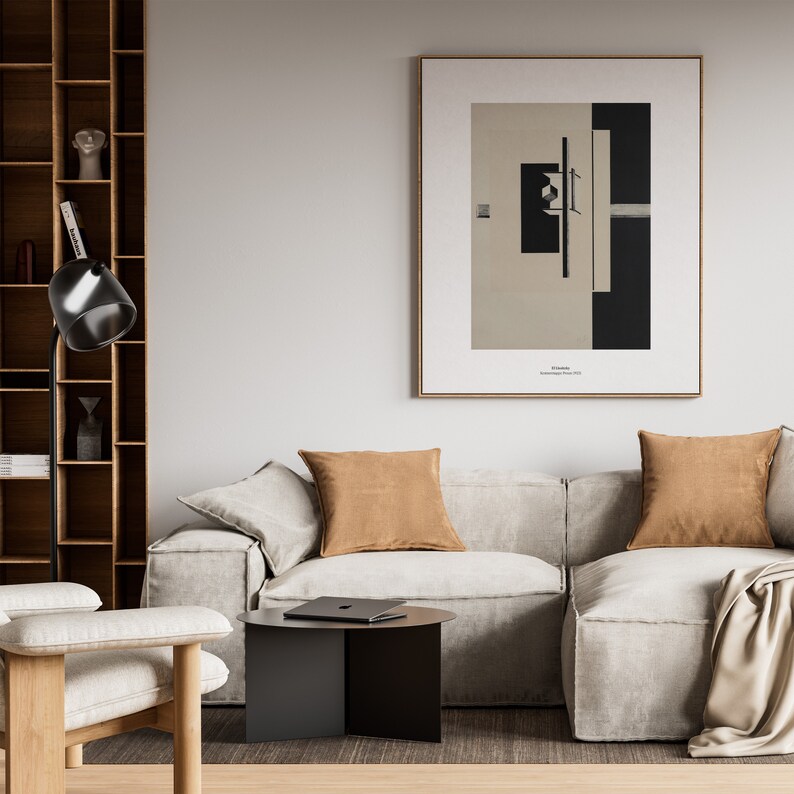 May include: A living room interior with a beige sectional sofa, two brown throw pillows, a black side table, a floor lamp, and a framed black and white abstract art print on the wall. The art print has the text "El Lissitzky, Proun 1923" below the image.