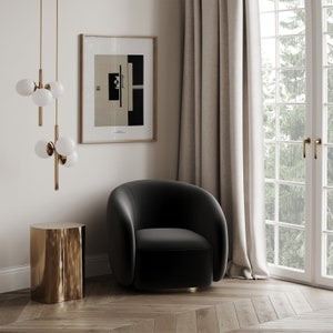 May include: A black velvet armchair with rounded edges sits in a room with a gold side table, a framed abstract print, and a window with white curtains.