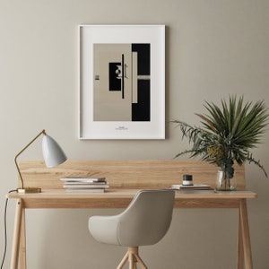 May include: A white desk with a wooden top and gold metal legs. A white lamp with a black cord is on the left side of the desk. A stack of books is on the desk. A white chair with wooden legs is in front of the desk. A vase with green plants is on the right side of the desk. A framed black and white abstract print is on the wall behind the desk.