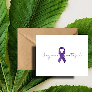 May include: A white card with a purple ribbon and the text "beyond grateful" in black cursive writing. The card is sitting on a brown envelope and green leaves.