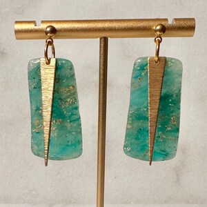 May include: A pair of gold and teal green earrings with a geometric design. The earrings are made of metal and glass.