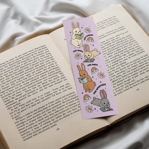 May include: A purple bookmark with illustrations of bunnies reading books, doing magic, and going on adventures. The bookmark has the text "Love Books", "Love Magic", and "Love Adventures" on it.