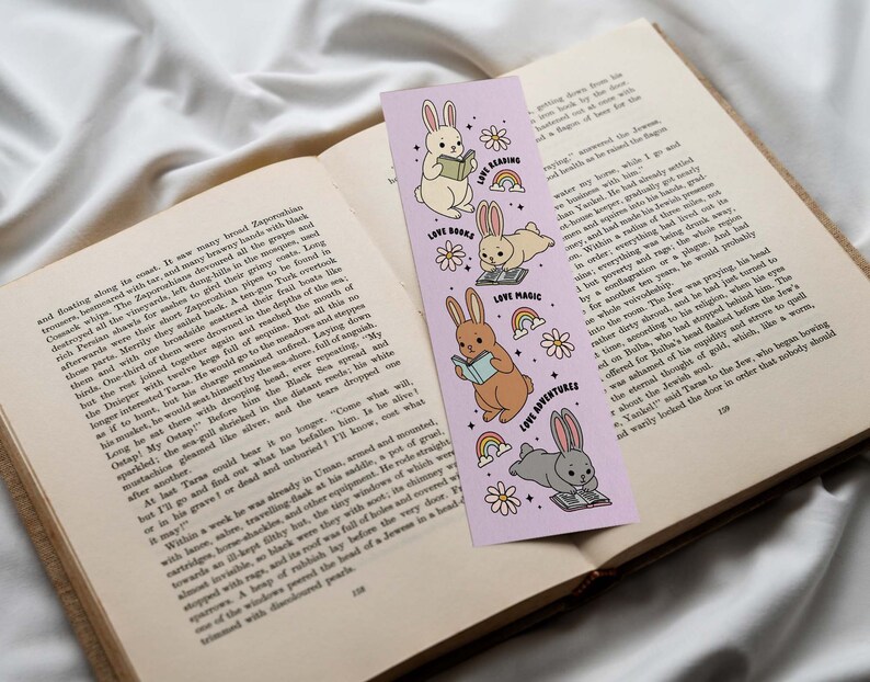 May include: A purple bookmark with illustrations of bunnies reading books, doing magic, and going on adventures. The bookmark has the text "Love Books", "Love Magic", and "Love Adventures" on it.
