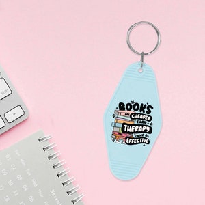 May include: A light blue motel key chain with the text "BOOKS ARE CHEAPER THAN THERAPY TWICE AS EFFECTIVE" and a stack of colorful books with a rainbow and clouds.