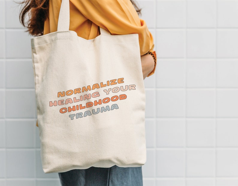 May include: A white canvas tote bag with the text "Normalize Healing Your Childhood Trauma" in colorful, stylized lettering.