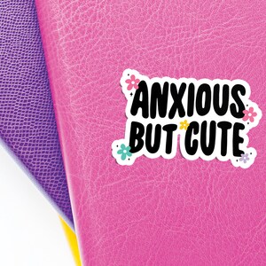 May include: A pink leather journal with a sticker that says "Anxious but cute" with colourful flowers around the text.