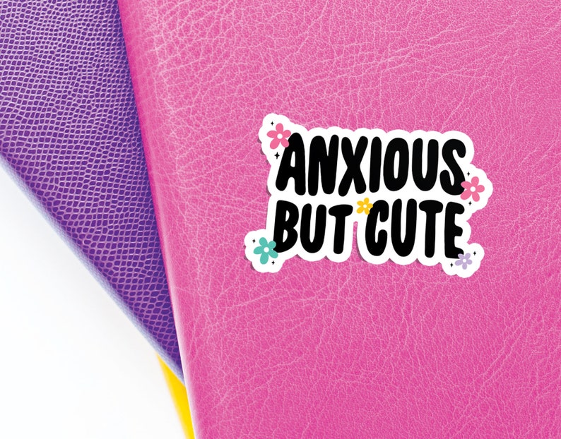 May include: A pink leather journal with a sticker that says "Anxious but cute" with colourful flowers around the text.