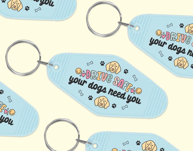 May include: Light blue key chain with a white and pink design. The keychain features a cartoon dog and the text "Drive Safe, your dogs need you".
