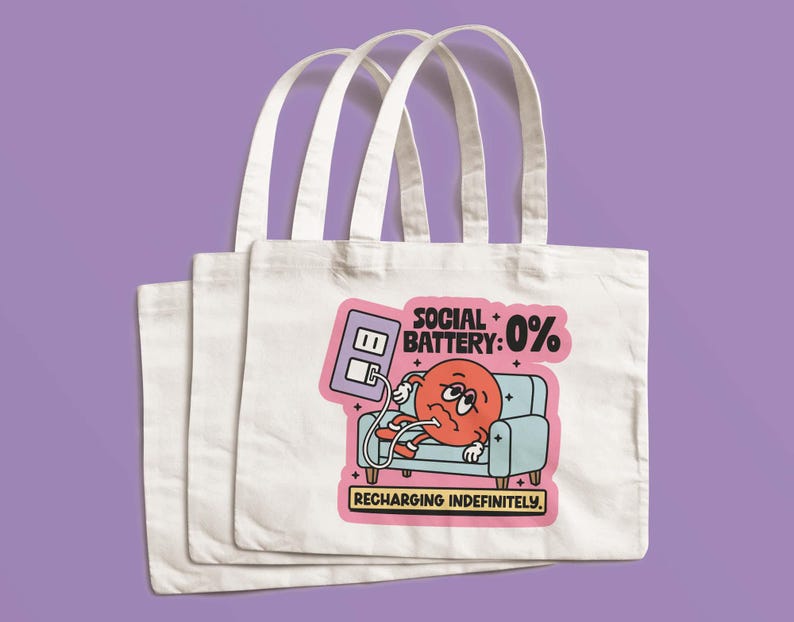 May include: Three white canvas tote bags with a colorful graphic. The graphic shows a cartoon character with a red face, plugged into a wall outlet, on a blue couch. Text reads "SOCIAL BATTERY: 0% RECHARGING INDEFINITELY."