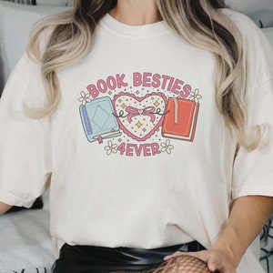 May include: White t-shirt with a graphic of two books tied together with a pink ribbon and a heart that says "Book Besties 4ever".