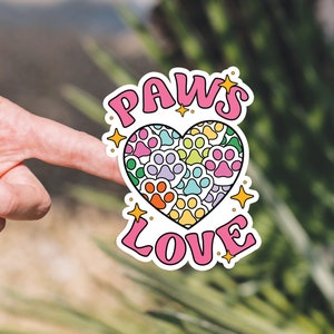 May include: A pink and white sticker with the words "PAWS LOVE" and a heart made of paw prints in rainbow colors.