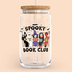 Puede incluir: Un tarro de vidrio transparente con tapa de madera y pajita. El tarro presenta un gr&aacute;fico colorido de personajes de Halloween de dibujos animados leyendo libros, con las palabras "Spooky Book Club" arriba y abajo de los personajes. El dise&ntilde;o incluye una parca, un fantasma, una bruja, un vampiro y un diablo.
