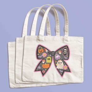 May include: Three white canvas tote bags with a Halloween design. The design features a black bow shape with a pink outline, and is filled with Halloween icons such as a pumpkin, ghost, and skull and crossbones.