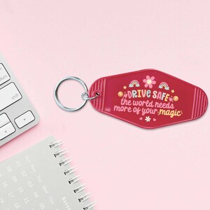 May include: A pink motel key chain with a white flower and rainbow design. The keychain says "DRIVE SAFE the world needs more of your magic".