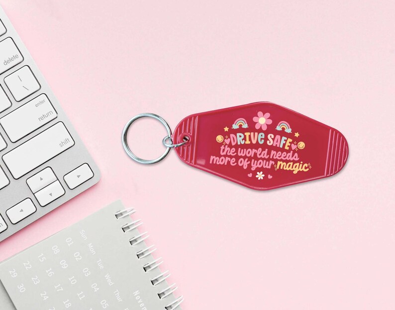 May include: A pink motel key chain with a white flower and rainbow design. The keychain says "DRIVE SAFE the world needs more of your magic".