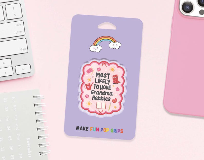 Może przedstawiać: Jasnofioletowy PopGrip z r&oacute;żowym i białym wzorem z napisem "MOST LIKELY TO HAVE Grandma Hobbies". PopGrip ma u g&oacute;ry tęczę i chmury i znajduje się na jasnofioletowym tle. Tekst "MAKE FUN POP GRIPS" znajduje się na dole.