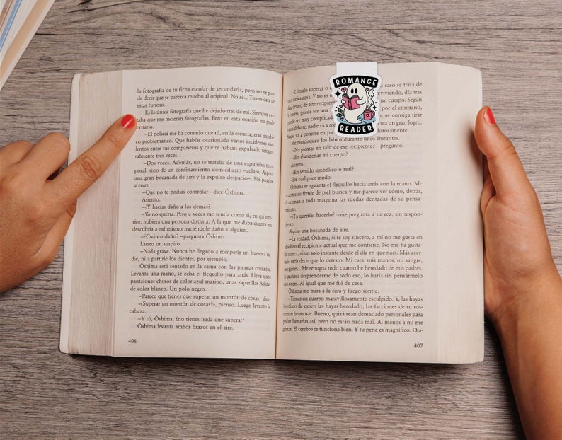 Op de afbeelding: Een close-up van een open boek met een bladwijzer met een spook dat een boek leest. Het boek is getiteld "Romance Reader". De tekst op de pagina luidt: "Que no te pod&iacute;as controlar -dice Oshima. -Y, Oshima, &iquest;tienes nada que superar? Oshima levanta ambos brazos en el aire."