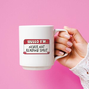 May include: White ceramic mug with a red and white name tag that says "Hello I'm Never Not Reading Smut".