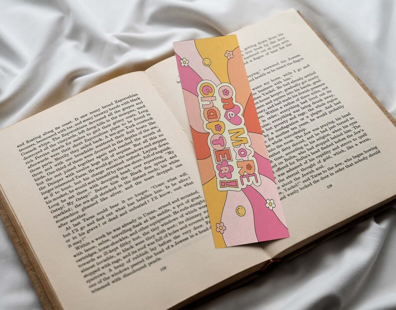 K&ouml;nnte beinhalten: Ein rosa und gelbes Lesezeichen im Retro-Design. Das Lesezeichen zeigt ein Herz mit dem Text "One More Chapter!" in einem wei&szlig;en Kreis. Das Lesezeichen ist mit Blumen und Schn&ouml;rkeln verziert.