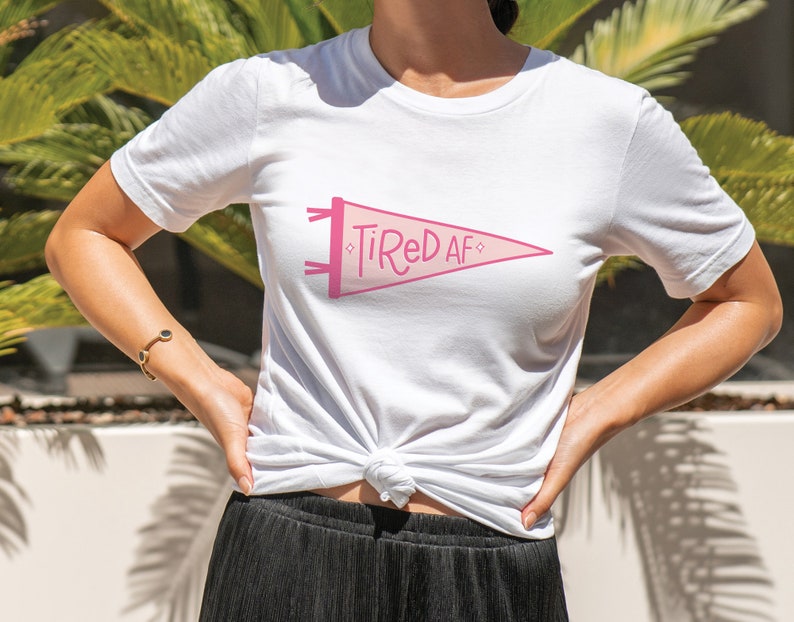 May include: White t-shirt with a pink pennant graphic that says "Tired AF".