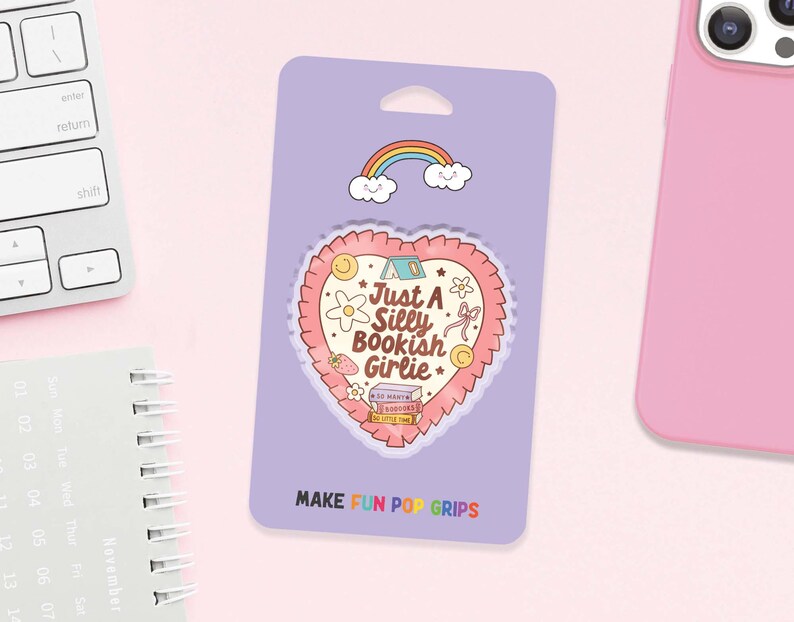 May include: A purple Pop Grip package with a heart-shaped design that reads "Just A Silly Bookish Girlie." The design includes a rainbow, clouds, flowers, and a strawberry. The text "MAKE FUN POP GRIPS" is at the bottom.