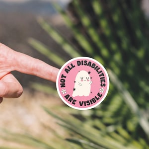 Op de afbeelding: Ronde roze sticker met een witte geest en de tekst "Not all disabilities are visible" met sterren en bloemen rond de geest.