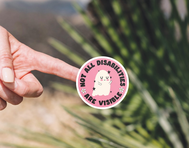 Op de afbeelding: Ronde roze sticker met een witte geest en de tekst "Not all disabilities are visible" met sterren en bloemen rond de geest.