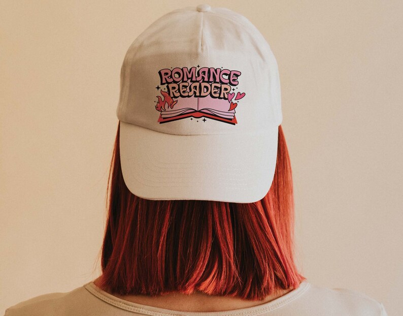 May include: White baseball cap with a pink and black graphic of a book with flames and the text "Romance Reader".