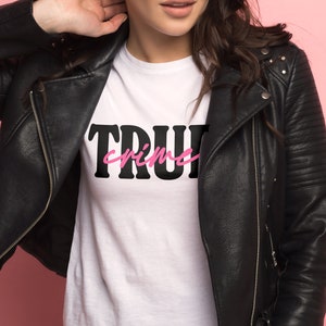 May include: A white t-shirt with black text that says "TRUE crime" in pink lettering. The shirt is being worn by a person wearing a black leather jacket.