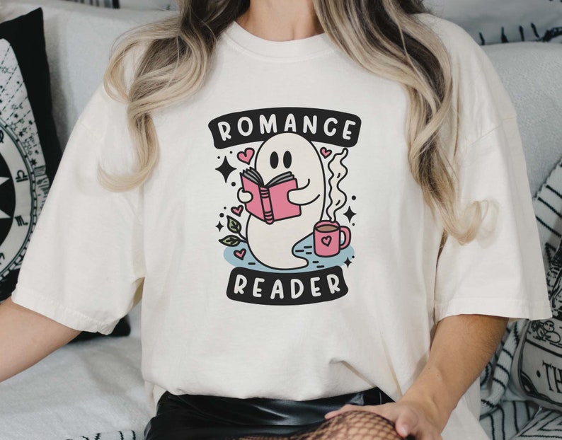Op de afbeelding: Wit T-shirt met een afbeelding van een geest die een boek leest en een kopje koffie vasthoudt. De tekst "Romance Reader" staat onder de geest.
