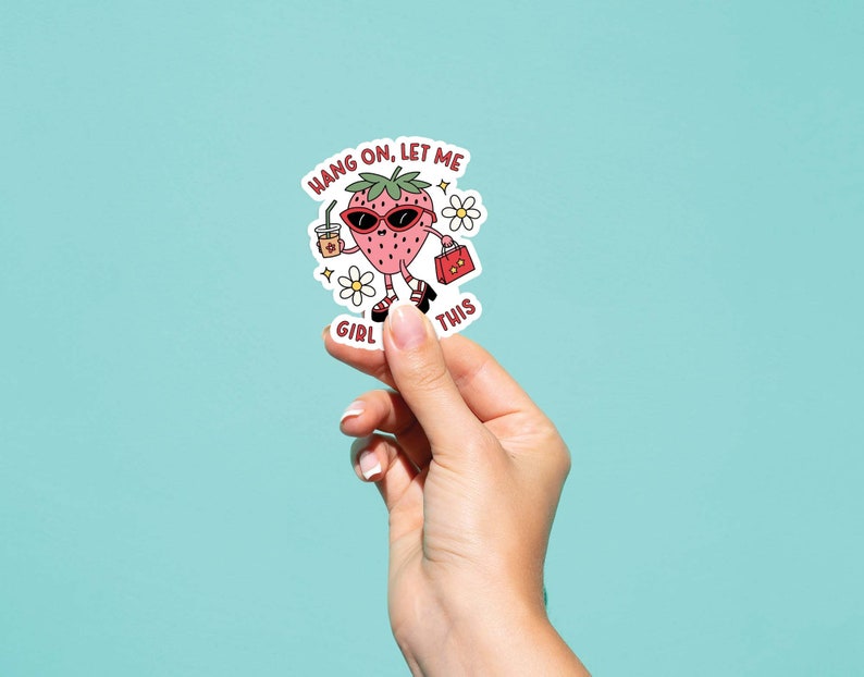 May include: A sticker featuring a cartoon strawberry wearing sunglasses and holding a drink and a purse. The text on the sticker reads "Hang on, let me girl this".