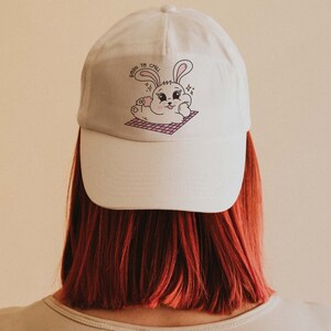 May include: White baseball cap with a pink and white bunny illustration and the text "Born to Chill".