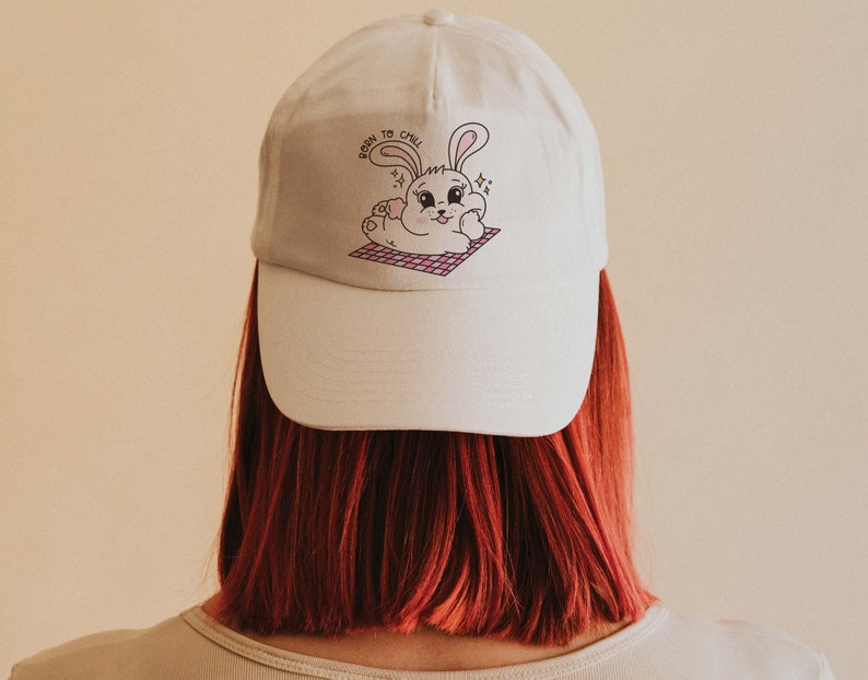 May include: White baseball cap with a pink and white bunny illustration and the text "Born to Chill".
