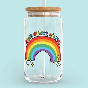 K&ouml;nnte beinhalten: Ein klares Glasgef&auml;&szlig; mit einem Holzdeckel und einem Regenbogenaufkleber mit der Aufschrift "Queer, All Day, All Year".