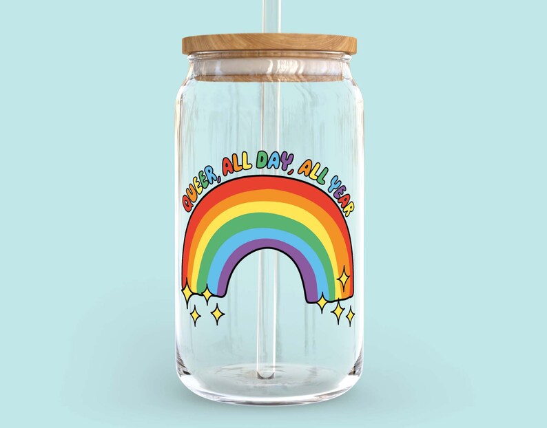 K&ouml;nnte beinhalten: Ein klares Glasgef&auml;&szlig; mit einem Holzdeckel und einem Regenbogenaufkleber mit der Aufschrift "Queer, All Day, All Year".