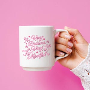 May include: White ceramic mug with a pink design that says "Very Demure, Very Mindful".