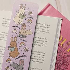 May include: A purple bookmark with illustrations of bunnies reading books. The bookmark has the text "Love Reading", "Love Books", "Love Magic", and "Love Adventures".