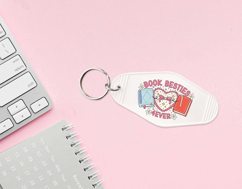May include: White motel key chain with a pink heart and two books tied together with a ribbon. The text on the keychain reads "Book Besties 4EVER".