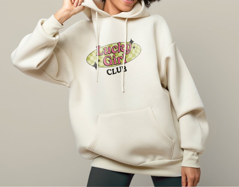 May include: A cream-coloured hoodie with a large graphic print of a retro-style oval with the text "Lucky Girl Club" in pink and green letters.