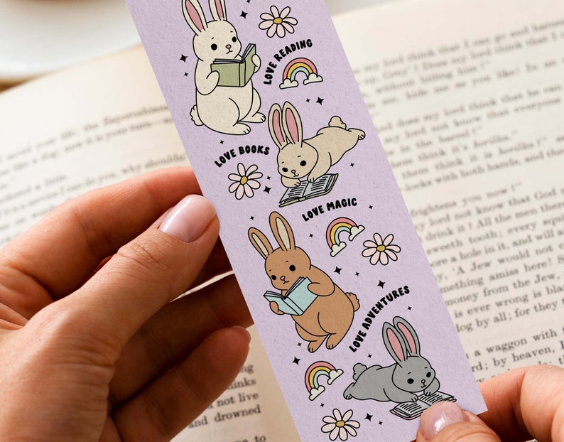 May include: A purple bookmark with illustrations of bunnies reading books. The bookmark has the text "Love Reading", "Love Books", "Love Magic", and "Love Adventures".
